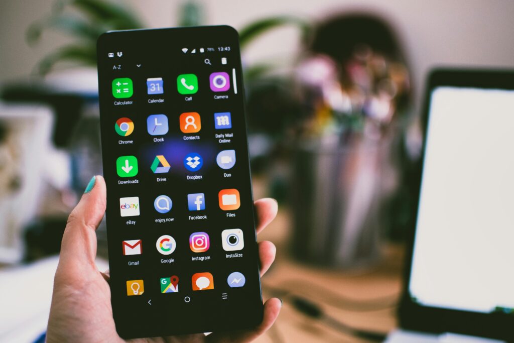 A close-up image of a person's hand holding a smartphone displaying various popular apps.